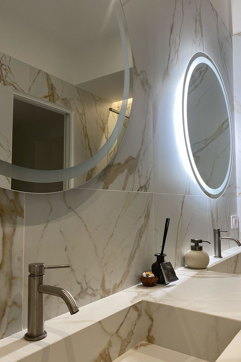 Il bagno consegnato: marmo e rovere con specchi tondi retroilluminati, identico al render